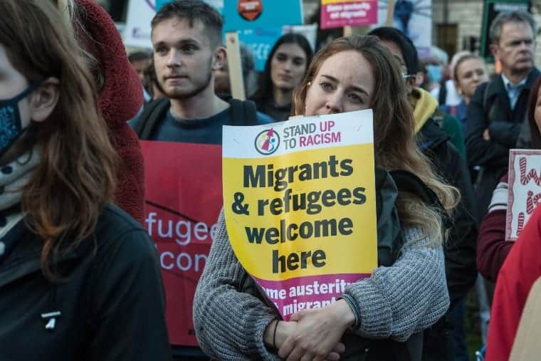 a person holds a sign that says migrants and refugees are welcome here