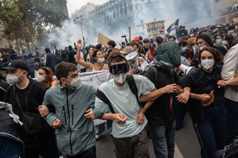 En France, des adolescents et des jeunes joignent les bras tandis que la police lance des grenades lacrymogènes pour tenter de disperser la foule.